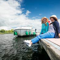 Two people wearing hats relaxing beside a river and boat in  Portumna, Co. Galway in Ireland's Hidden Heartlands.