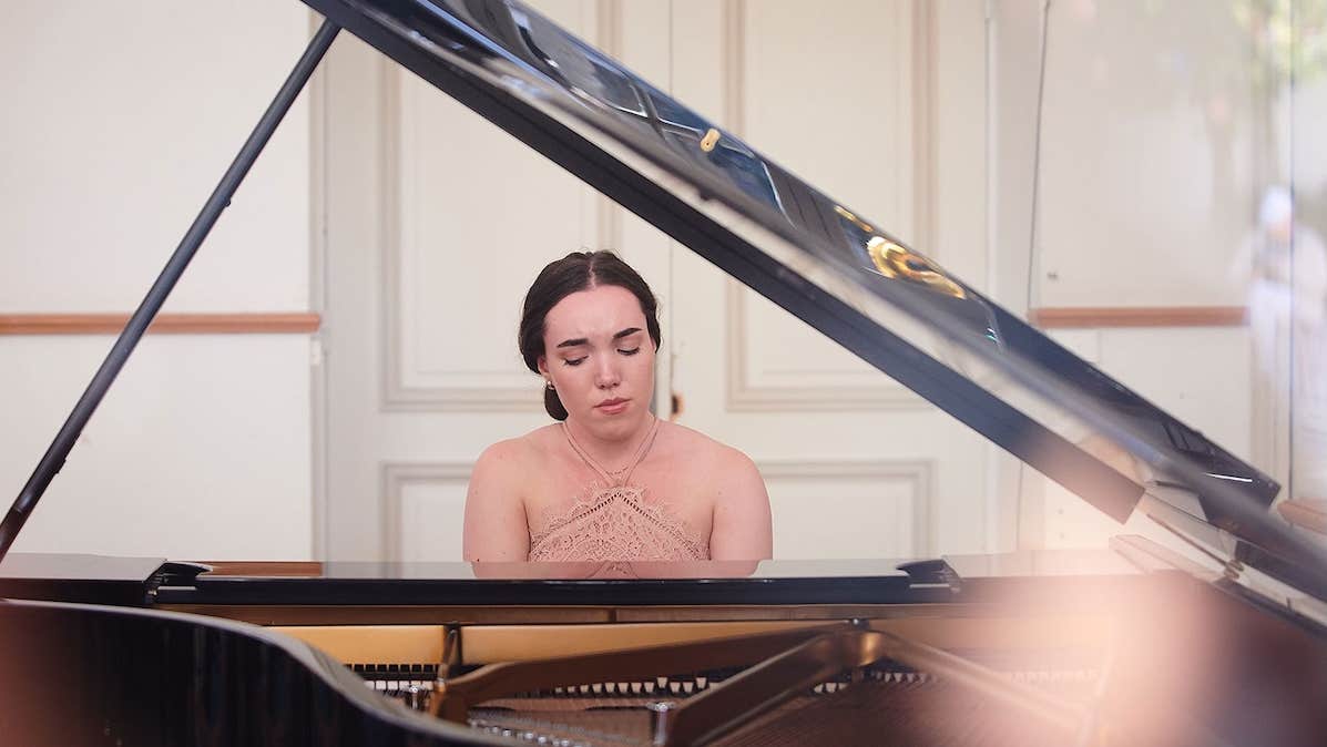 Looking through the open lid of grand piano at a woman playing at the keyboard.