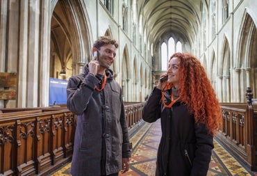 Two people listening to an audio guide device in a church aisle