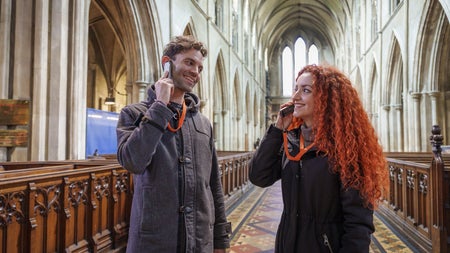 Two people listening to an audio guide device in a church aisle