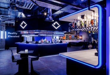 Blue neon lit stocked bar area with a table and two chairs