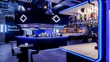 Blue neon lit stocked bar area with a table and two chairs