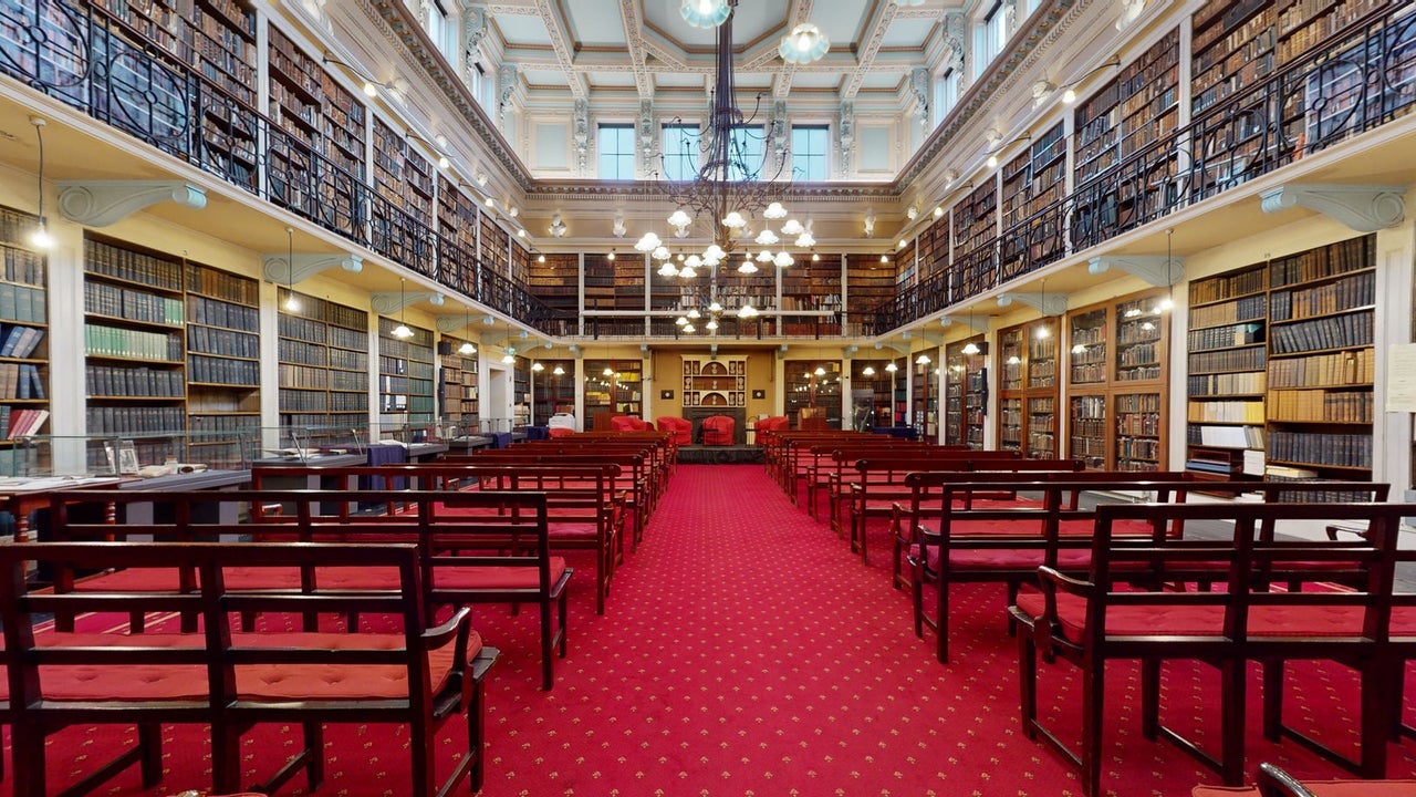 A library with wall to wall books and shelves with tables and chairs in a row 