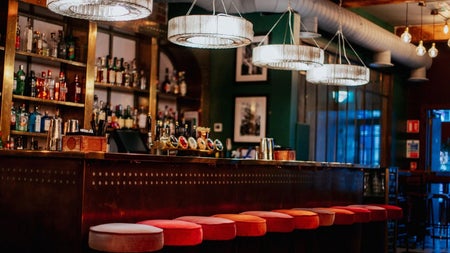 A bar counter with red covered stools and hanging lights