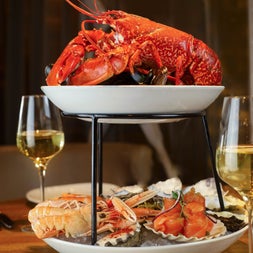 A tiered plate of lobster and lobster tails with two white wine glasses in the background