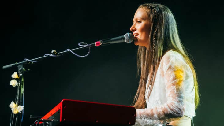 A woman is singing seated at a keyboard with a mic on a long arm in front of her.