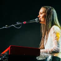 A woman is singing seated at a keyboard with a mic on a long arm in front of her.