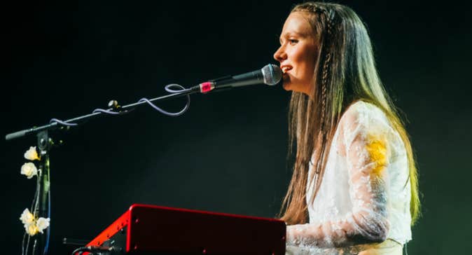 A woman is singing seated at a keyboard with a mic on a long arm in front of her.