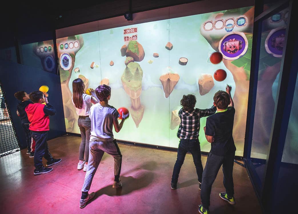 Children in a gaming room throwing balls at an interactive wall