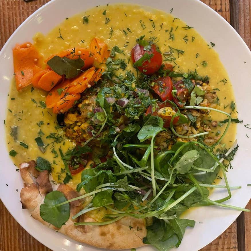 A white bowl with Dahl topped with carrots and other vegetables.