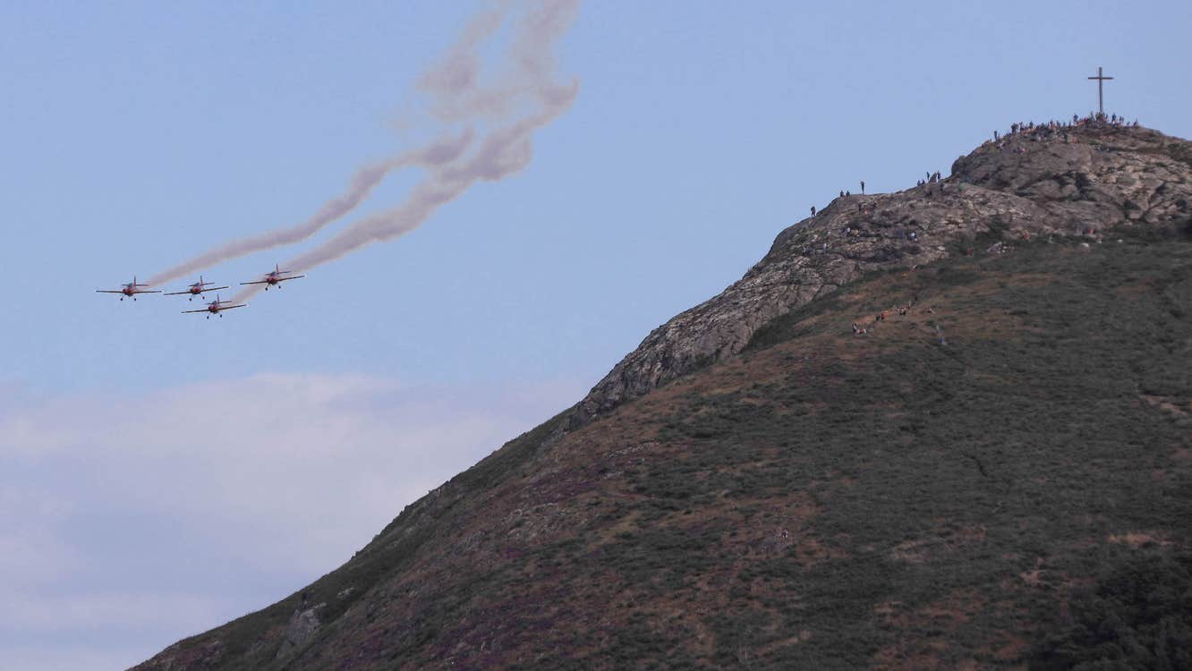 A hillside on the right hand side with 4 jets with smoke trails approaching from the distance.