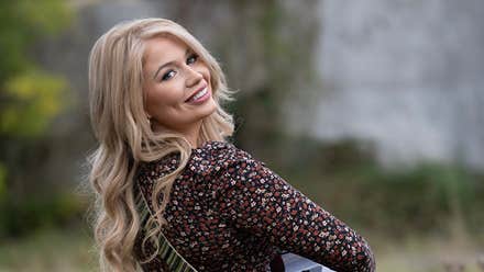 A smiling woman playing a guitar looking back over her right shoulder