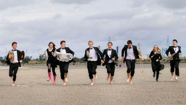 musicians running on Dollymount Strand with the Poolbeg Towers and blue skies behind them