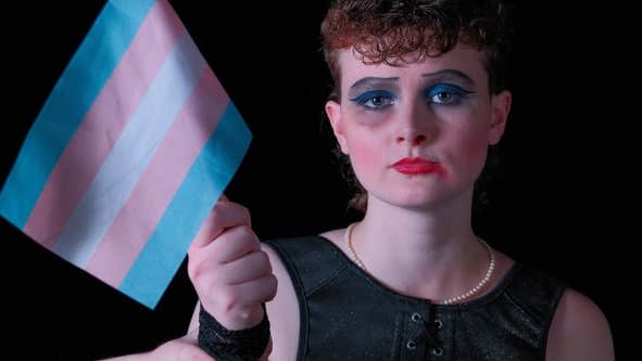 Roadkill Dublin Municipal Theatre at Smock Alley, a sad looking person wearing thick make-up, holding a small, stripy flag.