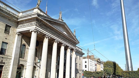 The General Post Office in Dublin with people walking nearby and the Spire in the background