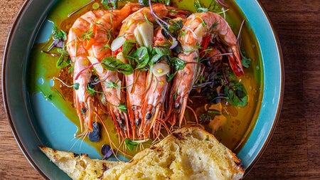 A plate of prawns in oil with fresh herbs alongside slices of toasted bread