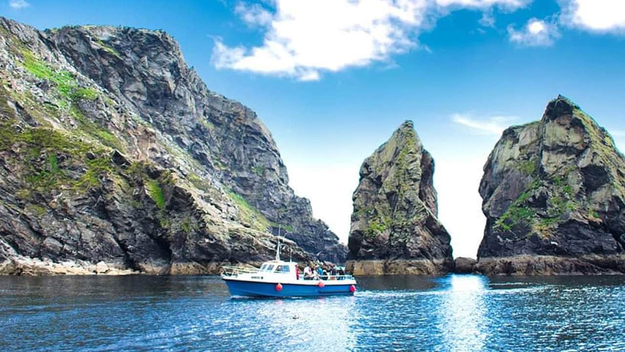 A blue boat out on the water with the sea cliffs in the background