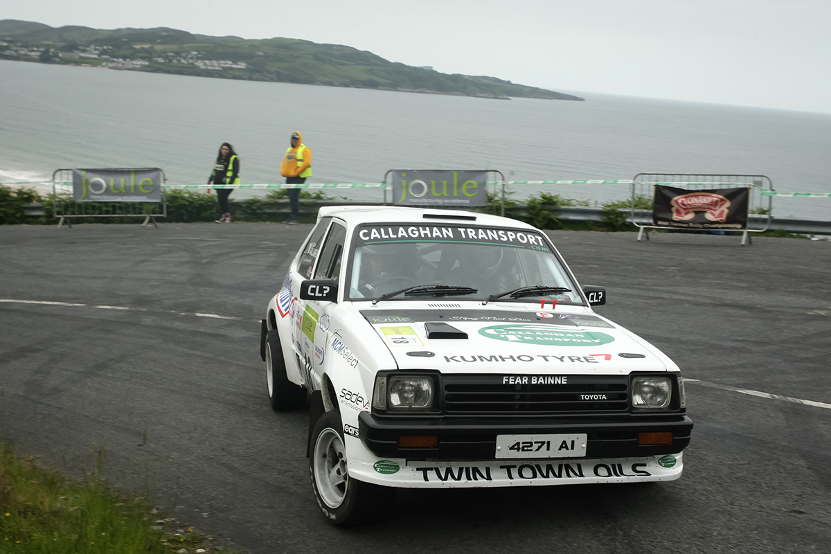 A white rally car is on road with the sea in the background