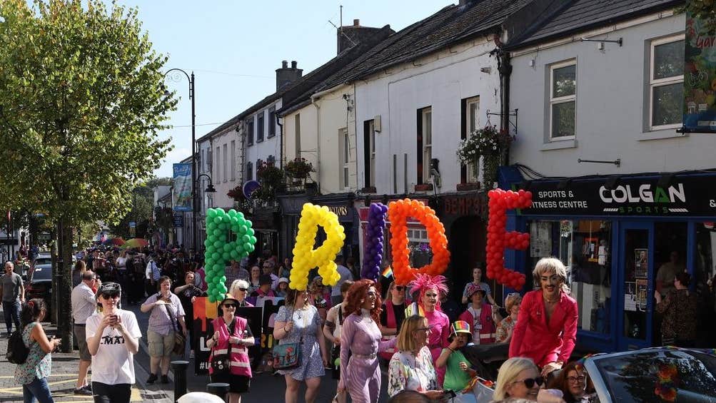 A parade is making it's way along a main street in a town with large different coloured letters made out of balloons.