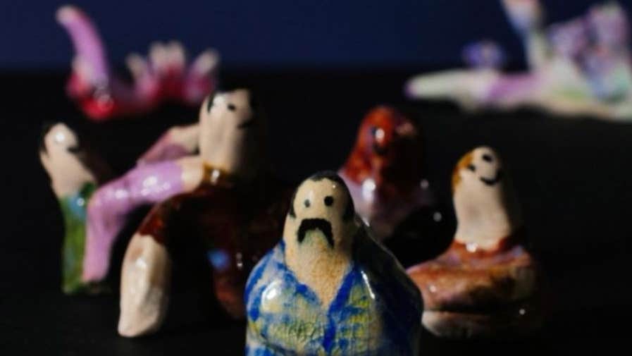 Out of focus image of small, roughly made painted ceramic figures against black background.