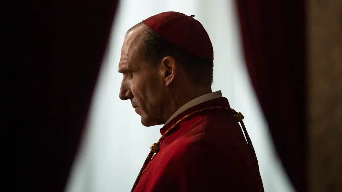 Side profile of a man in red church robes with small cap .