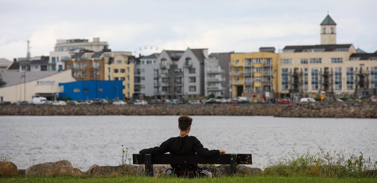 A man sitting on a bench along the Salthill Promenade in Galway city.