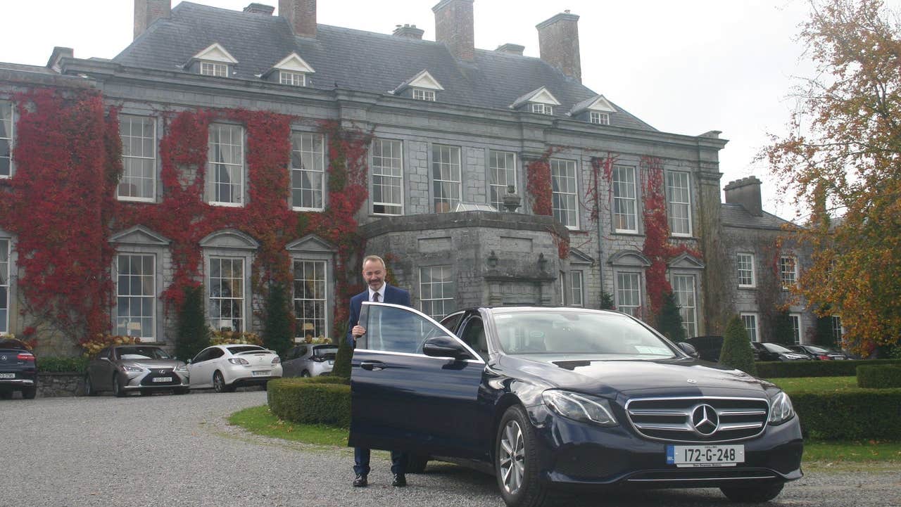 Man standing at car with ivy clad house in background