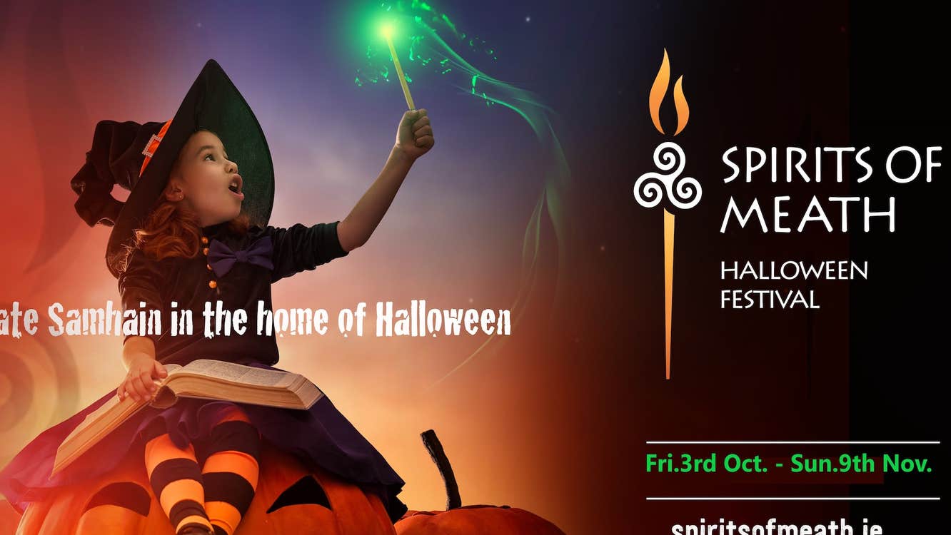 Child in witch's costume sitting on a large pumpkin holding up a wand with a green tip