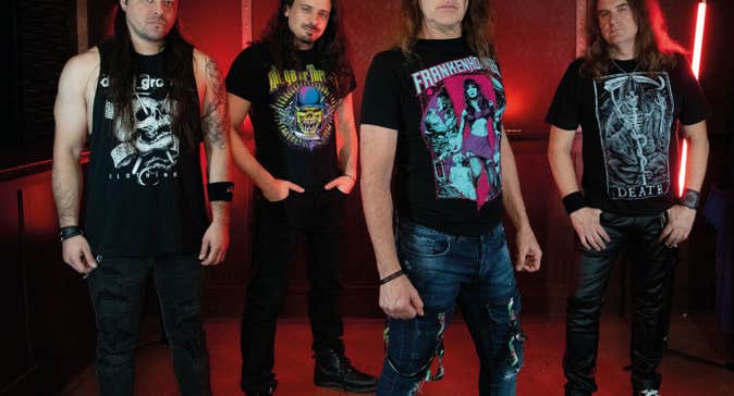 Group of 4 men in black T-shirts and long hair looking serious.