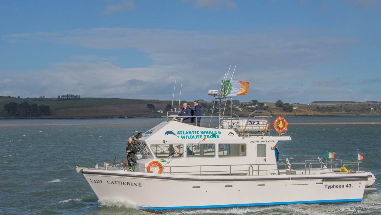 Three people on a white boat in Kinsale Harbour with the Irish flag flying