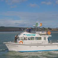 Three people on a white boat in Kinsale Harbour with the Irish flag flying