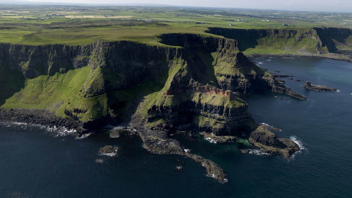 View of cliffs with flat green fields in the distance