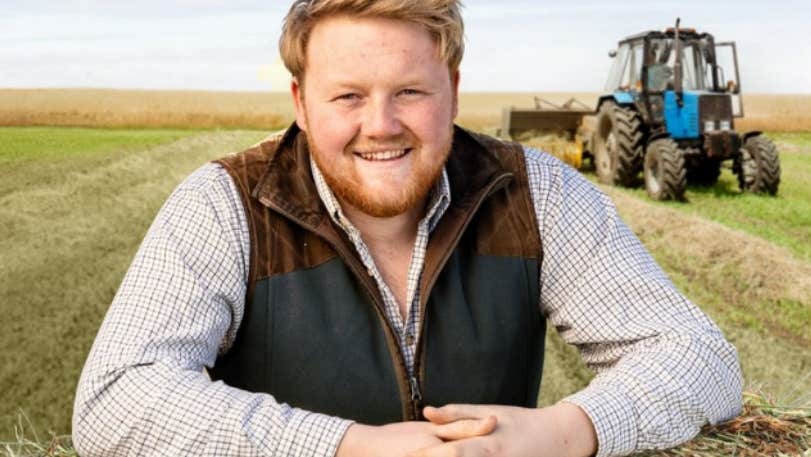 An Evening with Kaleb Cooper, a smiling man resting hands on bale with field behind him