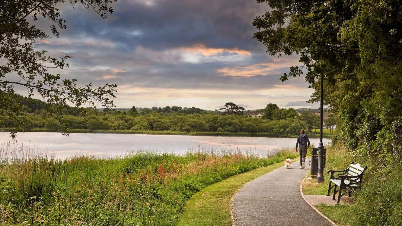 A person walking a dog along a lake side pathway