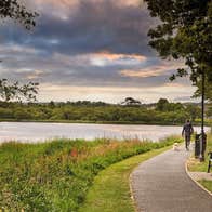 A person walking a dog along a lake side pathway