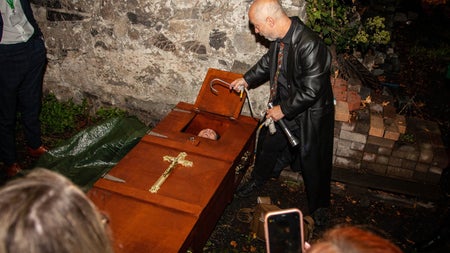A tour guide showing people a coffin with a person in it