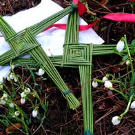 2 handmade green Brigid crosses on the ground with snowdrops and a white cloth