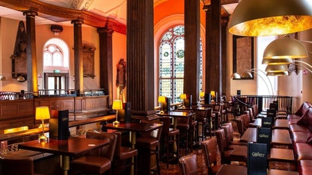 A bar with a seating area in a tall room with stained glass windows