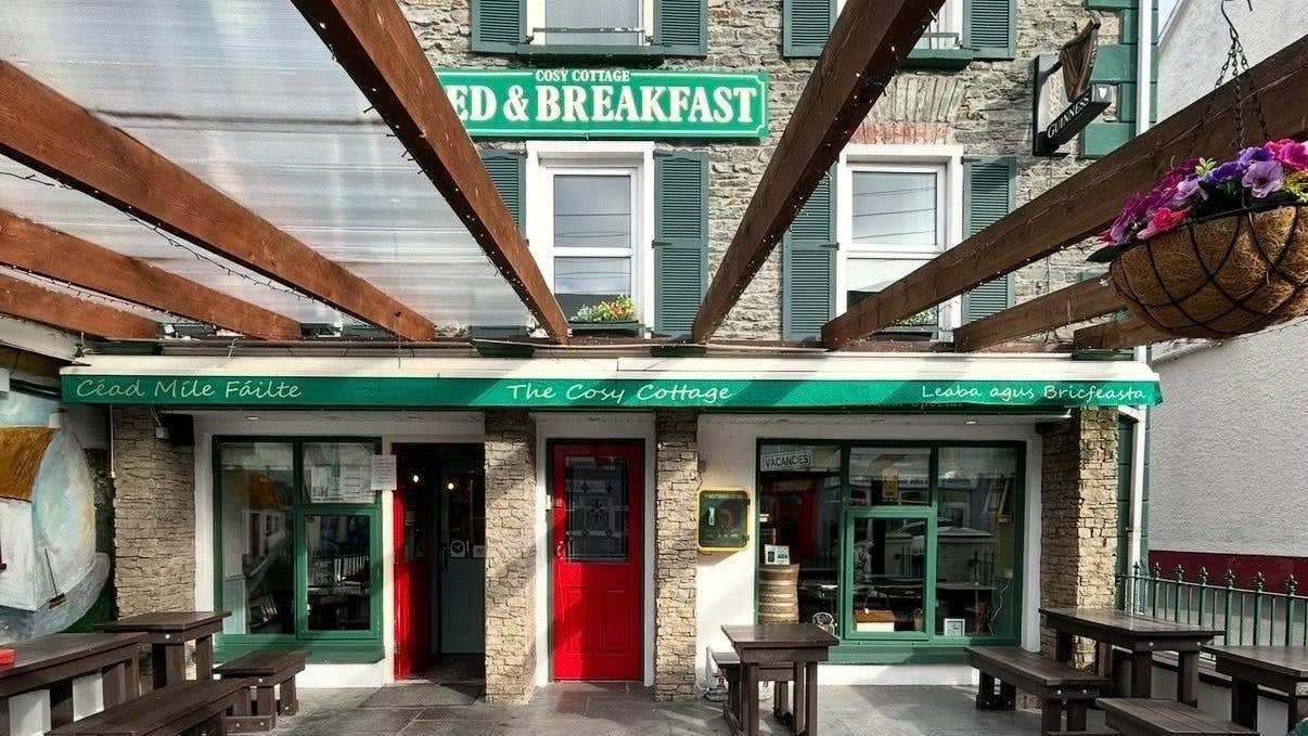 Exteriors of a coffee shop with a red door and green awning and benches in a courtyard
