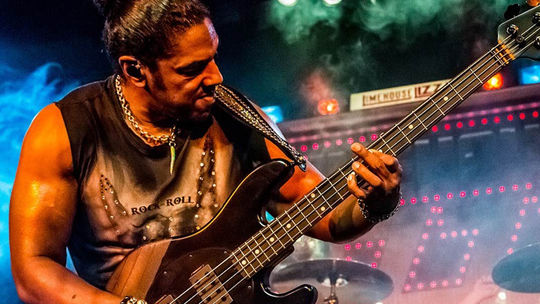 A man in leather trousers and gold jewelry is playing an electric guitar on a stage