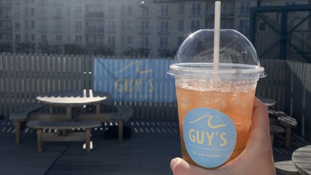 A hand holding up a take away cup with a cold drink from Guy's
