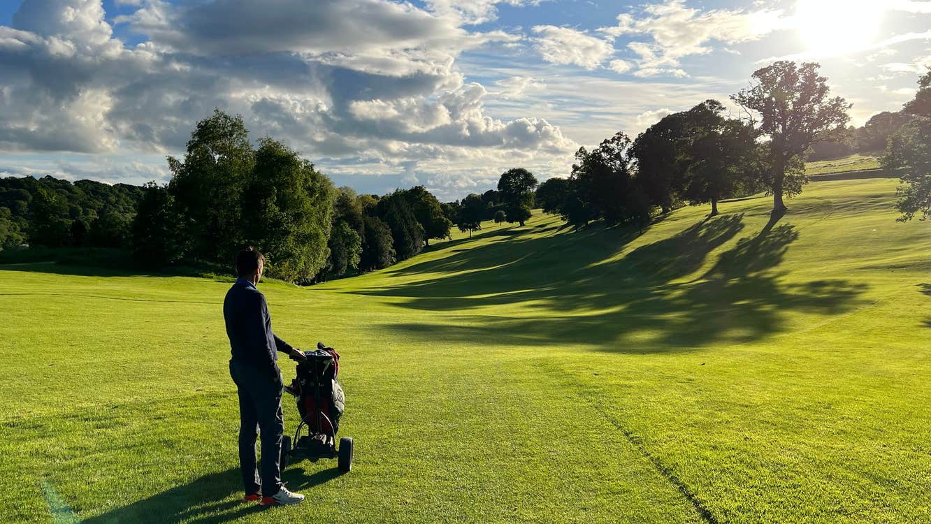 A golfer with his cart bag standing in the fairways of a golf course looking at the sunset