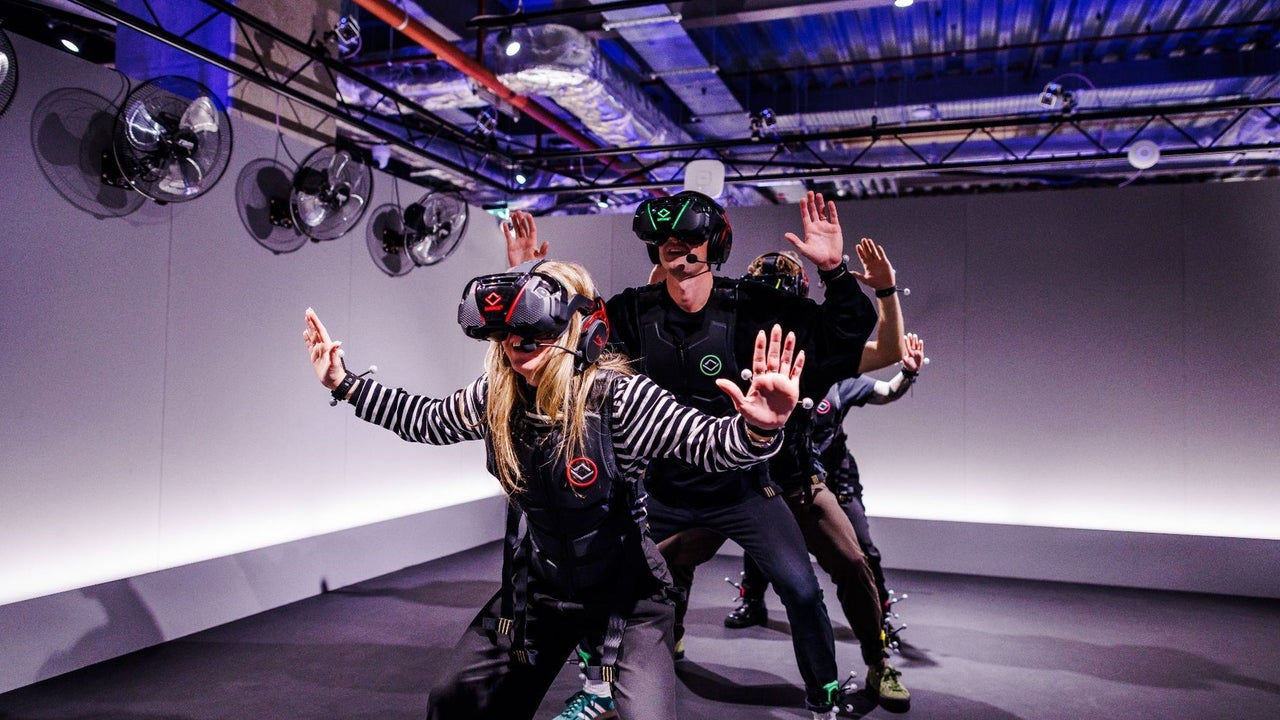 Four people wearing virtual reality headsets sanding in a line with their hands in the air