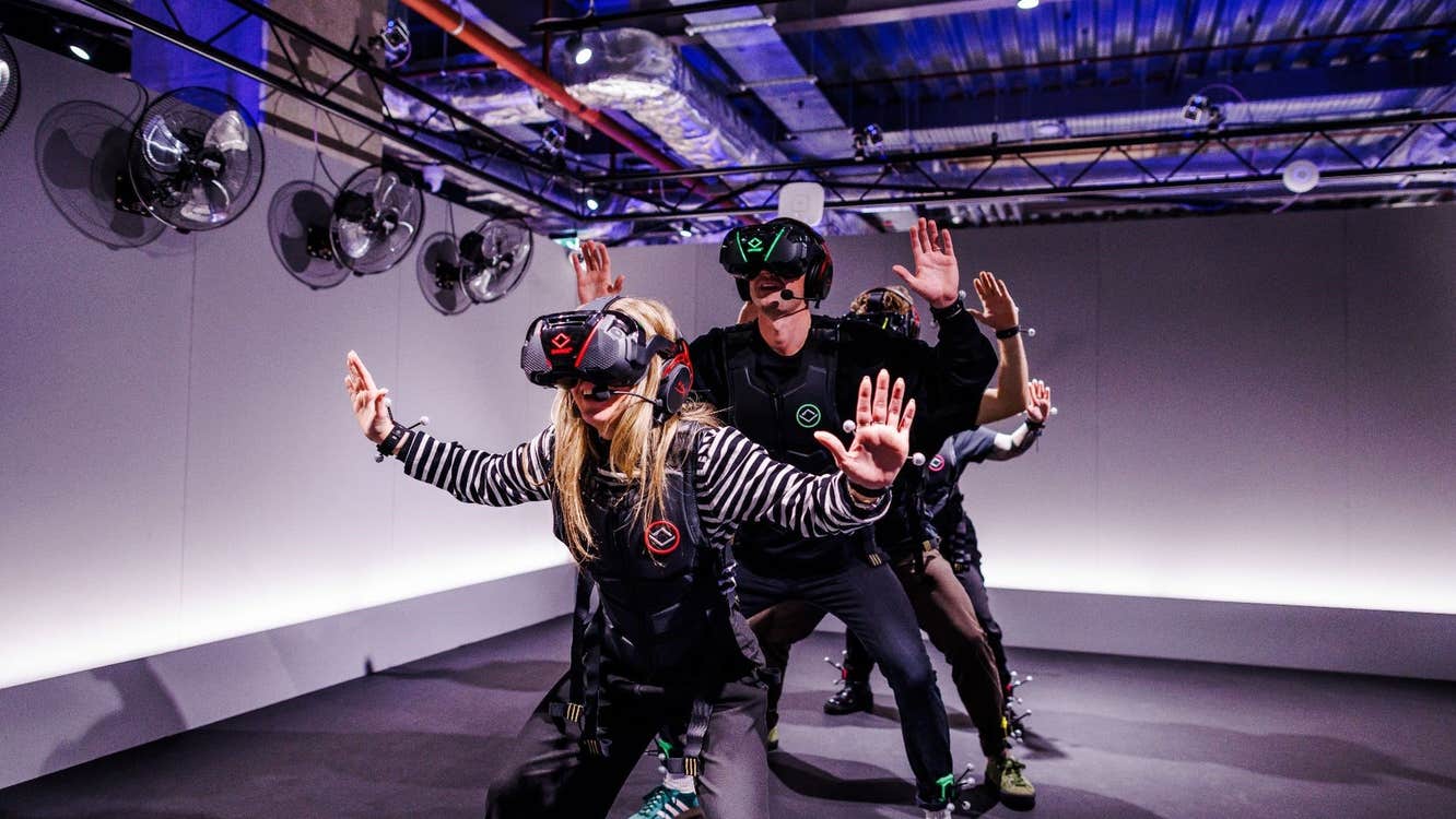 Four people wearing virtual reality headsets sanding in a line with their hands in the air