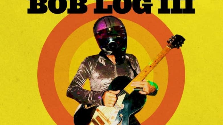 Bog Lob III poster in yellow with a man playing an electric guitar wearing a silver shirt and motorcycle helmet with black visor.
