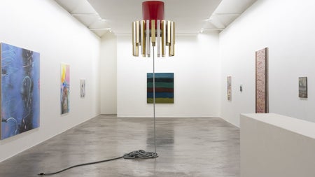 Art gallery displaying a gold and red lamp with an unplugged lead and paintings on the walls