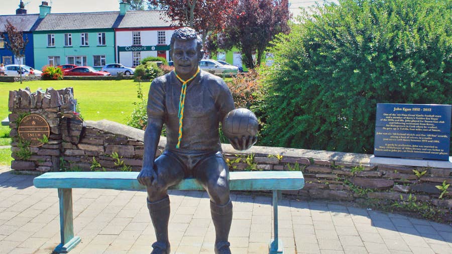 Bronze statue of footballer John Egan in seated pose with a football in hand