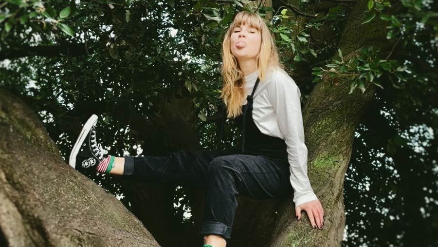 A woman is seating up a tree poking her tongue out.