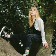 A woman is seating up a tree poking her tongue out.