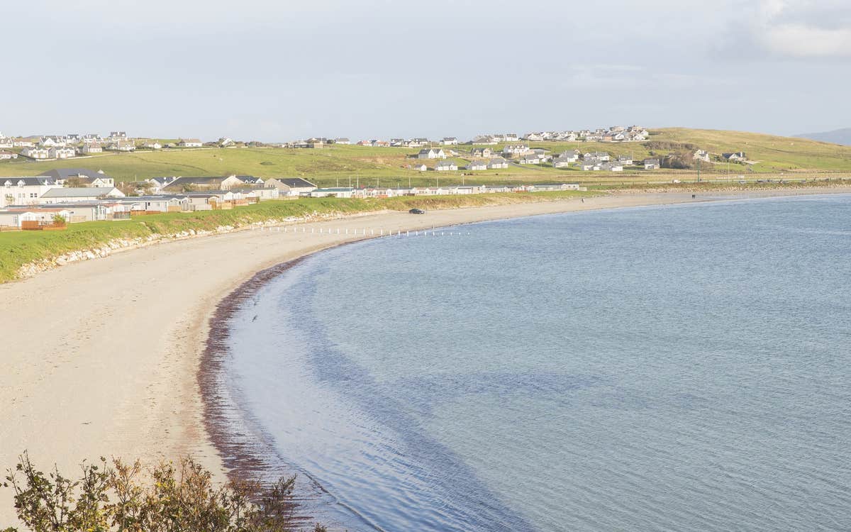 A picture of a curved beach with incoming tide and a village in the distance